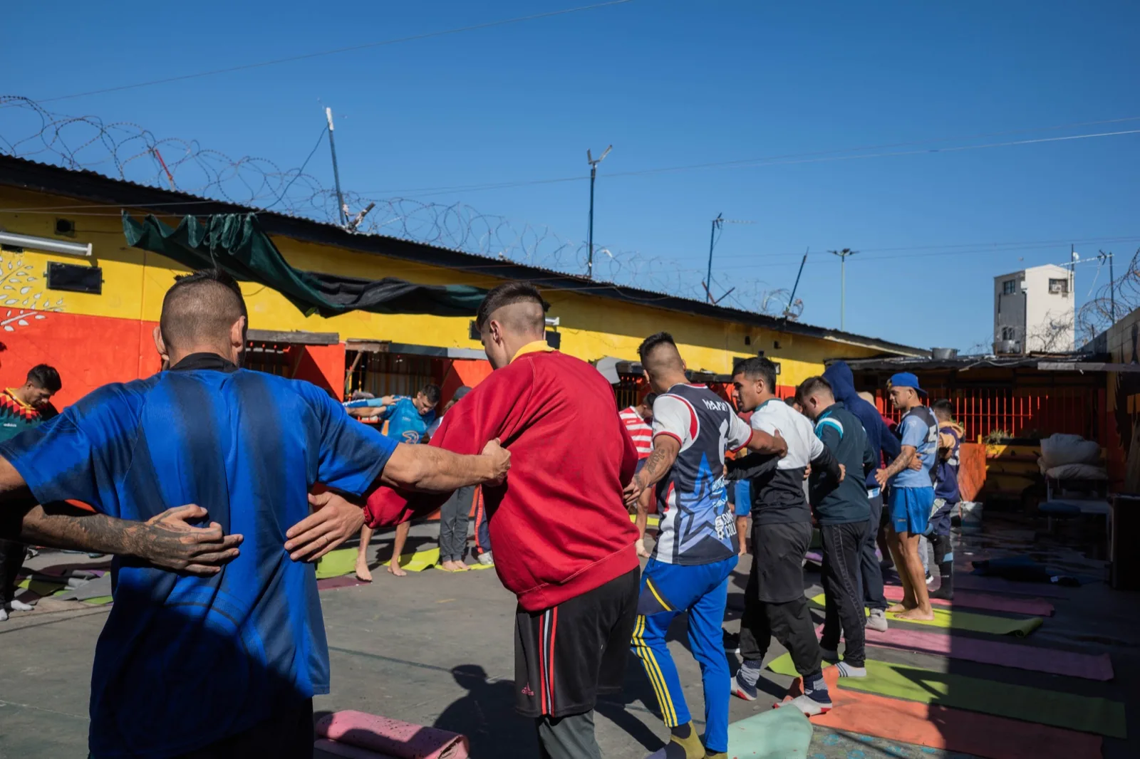 Clase al aire libre en el patio del penal: los alumnos en ronda, con las manos en los hombros del de adelante
