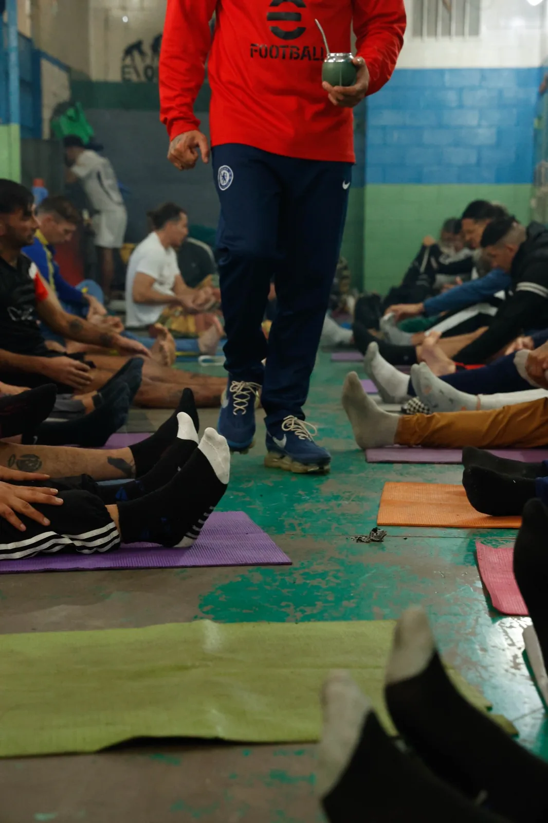 El profe recorre con el mate la fila de alumnos sentados en las colchonetas